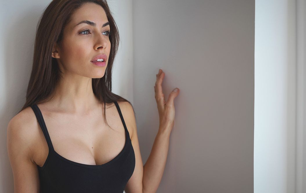 Woman standing by wall, looking thoughtfully away.