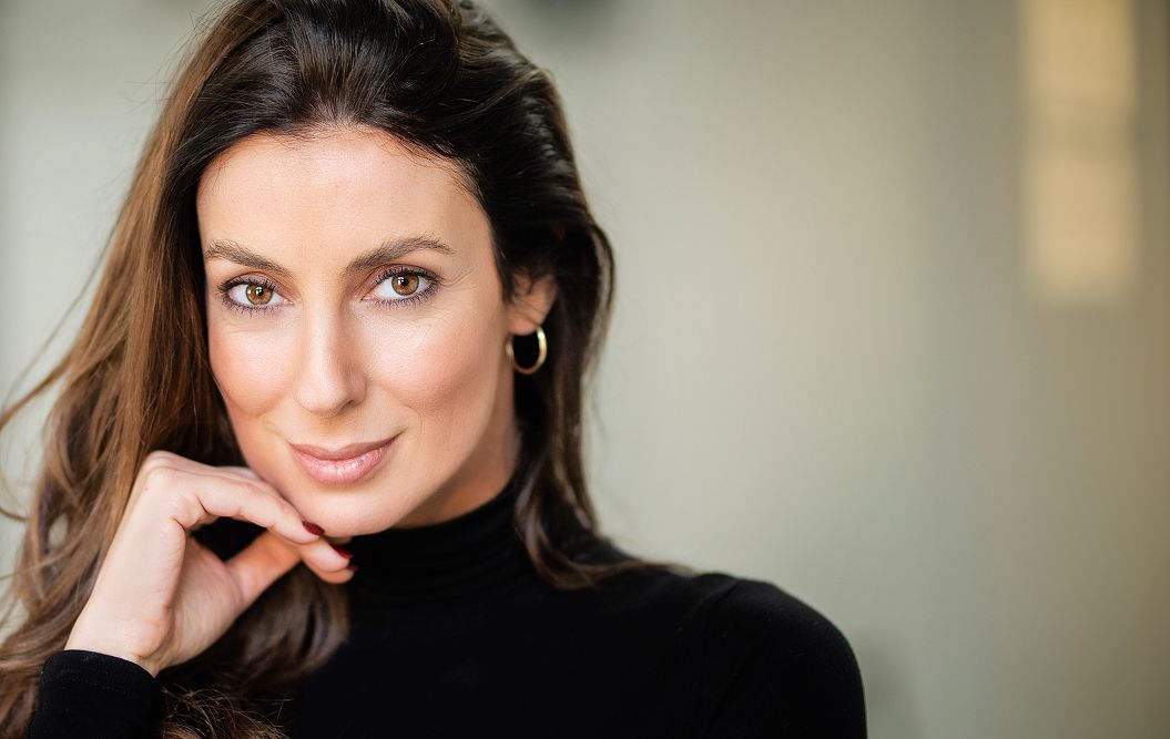 Woman with long hair smiling thoughtfully indoors.